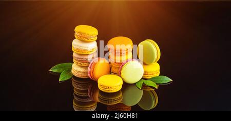 Sweet and colorful french macaroons.Banner of multicolored macaroons on a black background with fresh leaves.Kopy space. Stock Photo