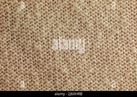 Beige knitted carpet close-up. Textile texture on a beige background. Detailed background from warm yarn. Natural wool fabric, sweater fragment. Stock Photo