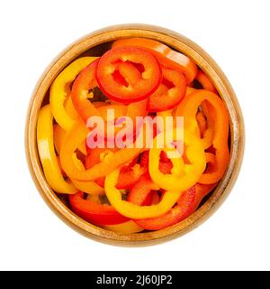 Sliced snacking mini sweet peppers, in a wooden bowl. Cross sections of ripe and fresh bell peppers, also called capsicums. Fruits of Capsicum annuum. Stock Photo