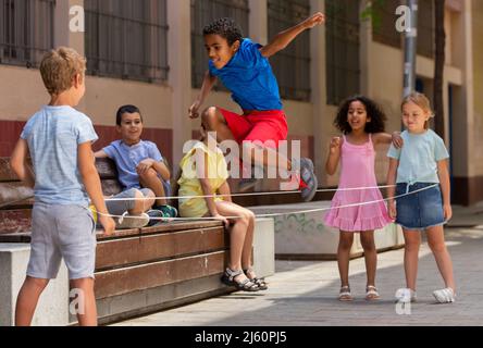 Energetic kids playing and skipping on elastic jumping rope in yard Stock Photo