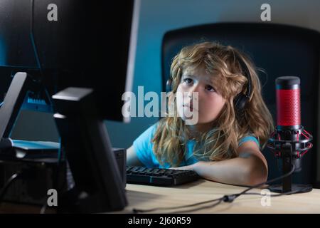 A little boy child uses a desktop at night, a child with computer screen in the room with neon lightning. Portrait of cute child while typing on Stock Photo