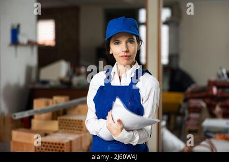 Positive female civil engineer taking notes while checking indoor construction site, satisfied with progress of work Stock Photo