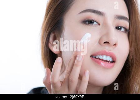 Beautiful young lady smears her face with an essential lotion, on white background - stock photo Stock Photo
