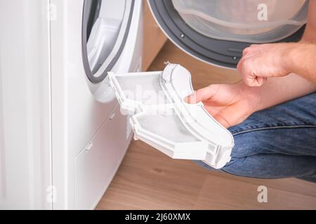 A man takes a lint filter out of the dryer and cleans it from dust, lint, hair, wool. Stock Photo