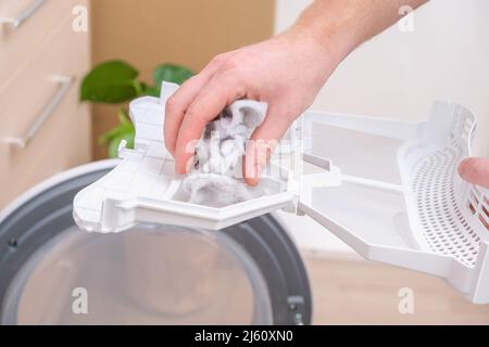 A man takes a lint filter out of the dryer and cleans it from dust, lint, hair, wool. Stock Photo
