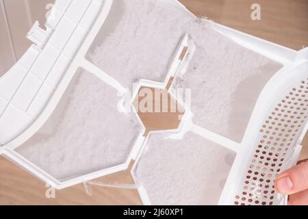 A man takes a lint filter out of the dryer and cleans it from dust, lint, hair, wool. Stock Photo