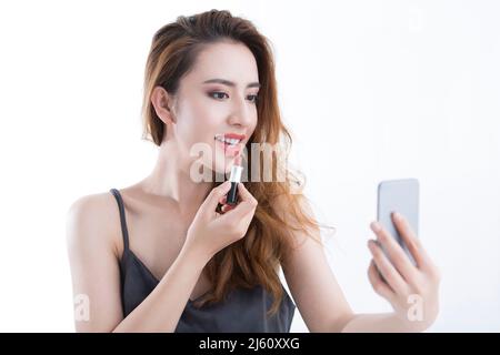 Beautiful young lady applying lipstick with a makeup mirror , on white background - stock photo Stock Photo