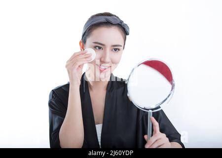 Young beauty looking at herself in a mirror is using a powder to make up, on white background - stock photo Stock Photo