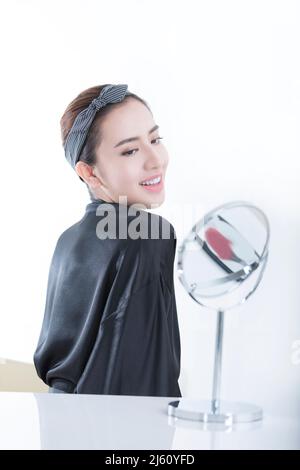 An elegant young Chinese woman looking at her shoulders in a makeup mirror, on white background - stock photo Stock Photo