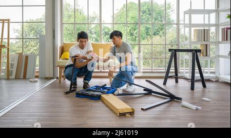 Two asian carpenters installing wooden bench in new house. House renovation service. Morning work atmosphere in the living room. Stock Photo