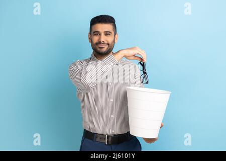 Portrait of smiling happy satisfied businessman throwing out his optical glasses after vision treatment, looking at camera, wearing striped shirt. Indoor studio shot isolated on blue background. Stock Photo