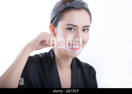 Beautiful young Chinese woman using a toothbrush to clean and whitening her teeth, on white background - stock photo Stock Photo