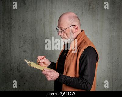 Head and shoulders portrait of a senior, bald and bearded man writing notes and sketching on a clipboard Stock Photo