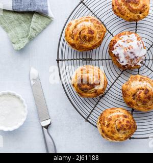 Top down view of cinnamon buns on a cooling rack served with cream cheese icing. Stock Photo