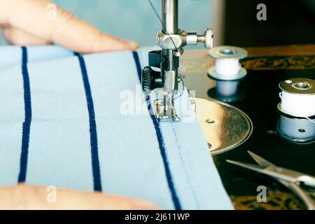 Cheerful woman sewing while sitting at her working place in fashion workshop. factory production of clothing. Stock Photo