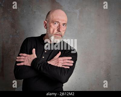 Head and shoulders portrait of a bald, bearded, thoughtful senior man in a black shirt Stock Photo