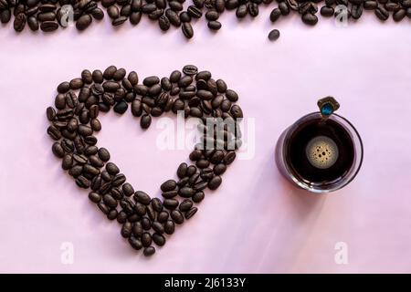Glass coffee mug and roasted coffee beans on a pink background. Coffee mania, love of coffee, concept. Heart from beans. top view Stock Photo
