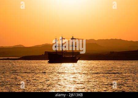 An old sailboat sailing against the background of a yellow sunset. Beautiful summer landscape. A yacht in the style of an old medieval sailboat. Stock Photo