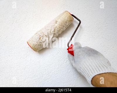 Male hand painting wall with paint roller. Renovating with white color paint. Stock Photo