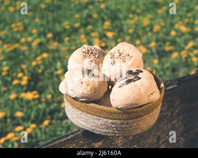 rustic crusty buns decorated with sesame and pumpkin seeds on garden fence in front of flower meadow. layout with free copy (text) space. Stock Photo