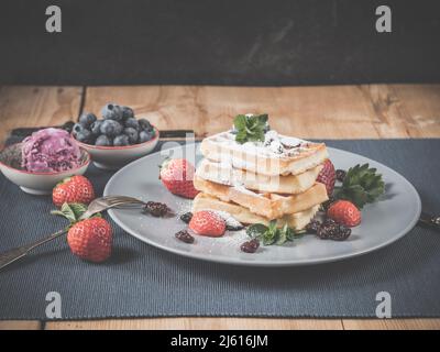photo shows traditional homemade fresh baked waffles decorated with sugar powder, fresh picked blueberries, strawberries, mint garnished with homemade Stock Photo