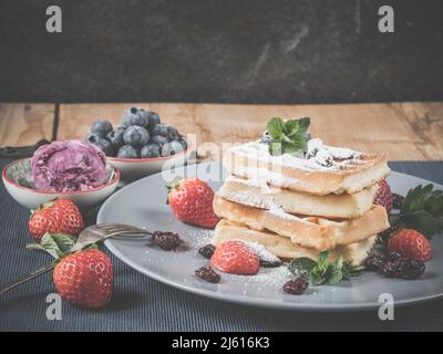 photo shows traditional fresh baked homemade waffles decorated with sugar powder, fresh picked blueberries, strawberries, cranberries, mint garnished Stock Photo