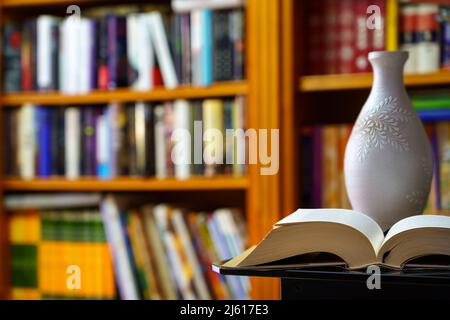 library with many books to read, arranged on shelves. Open book and vase in the foreground. Copy space. Background. Stock Photo
