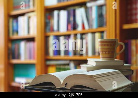 library with many books to read, arranged on shelves. Open book and cup close-up. Copy space. Background. Stock Photo