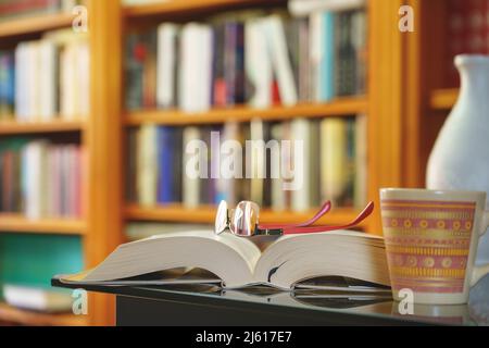 library with many books to read, arranged on shelves. Open book, glasses and mug close-up. Copy space. Background. Stock Photo