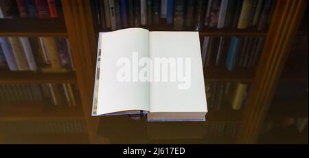 Blank open book to write your text, on a glass table with a reflection of the bookcase on the back. Copy space. Background. Stock Photo