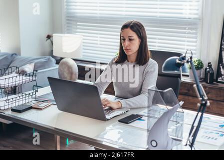 Side view of young woman working in office sitting and using laptop. Stock Photo