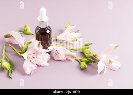 moisturizing liquid oil for the face, a cosmetic natural product in a bottle with a pipette made of glass a background of flowers alstroemerieae Stock Photo