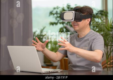 Asian man wearing VR headset and using laptop while sitting at his desk Stock Photo