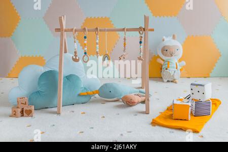 Baby activity gym play toys hanging from wooden arch on playmat in nursery or playroom. Home decoration children objects with learning cubes, plush Stock Photo