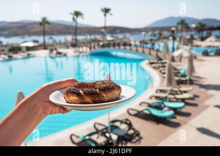 Turkish bagel on a saucer in hand against the backdrop of the blue sea and palm trees. National character.