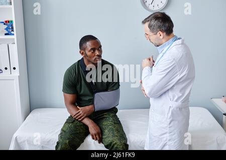Mature Caucasian traumatologist telling young African American military officer about broken arm treatment Stock Photo