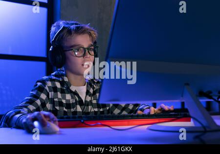 Young gamer boy with headphones playing computer video game. Stock Photo