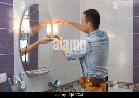 Handsome young builder is twisting the light bulb in. The man is looking up. Stock Photo