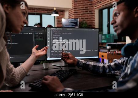 Network developers updating firewall system through information processing using multiple layers of security. Company programmers standing near desk with multiple monitors on top of it. Stock Photo