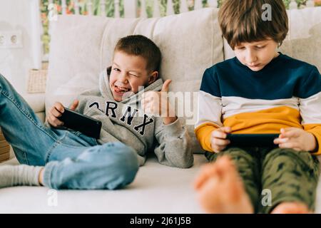 Cheerful two Childs boys playing online game, watching video on cellphone. Smiling kids using funny mobile apps, enjoying free leisure time at home on Stock Photo
