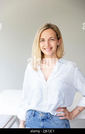 portrait of pretty young blonde business woman standing by her ergonomic height adjustable work desk in her home office Stock Photo