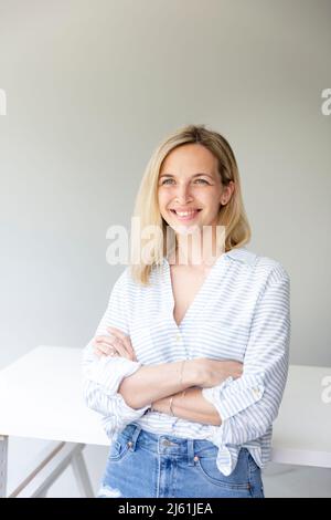 portrait of pretty young blonde business woman standing by her ergonomic height adjustable work desk in her home office Stock Photo