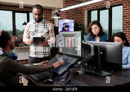 Game industry developer with multiple displays on desk working on level design and environment. Production department employees in office workspace developing videogame technology. Stock Photo