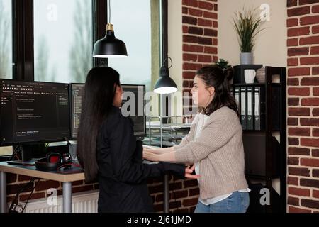 Company programmers standing near desk with multiple monitors on top of it. Network developers updating firewall system through information processing using multiple layers of security. Stock Photo