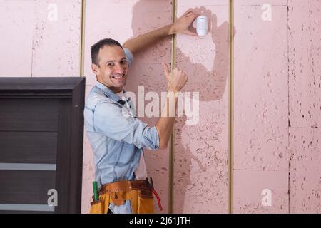 Young electrician installing security alarm on wall. Stock Photo