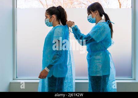 Nurse helping doctor in wearing protective workwear in clinic Stock Photo