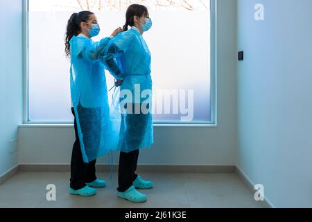 Nurse helping doctor in wearing protective workwear in hospital Stock Photo
