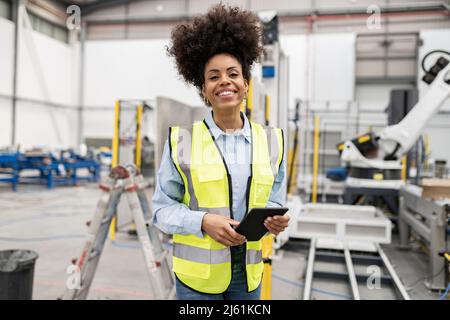 Happy technician holding tablet PC standing in factory Stock Photo