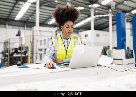 Engineer using laptop at desk in factory Stock Photo