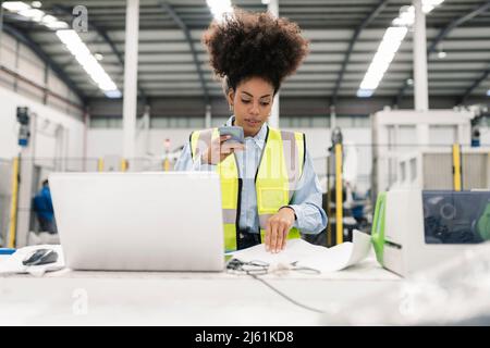 Engineer talking on mobile phone through speaker examining documents in factory Stock Photo